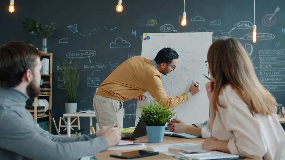 A man presenting a process on a whiteboard to colleagues in an office