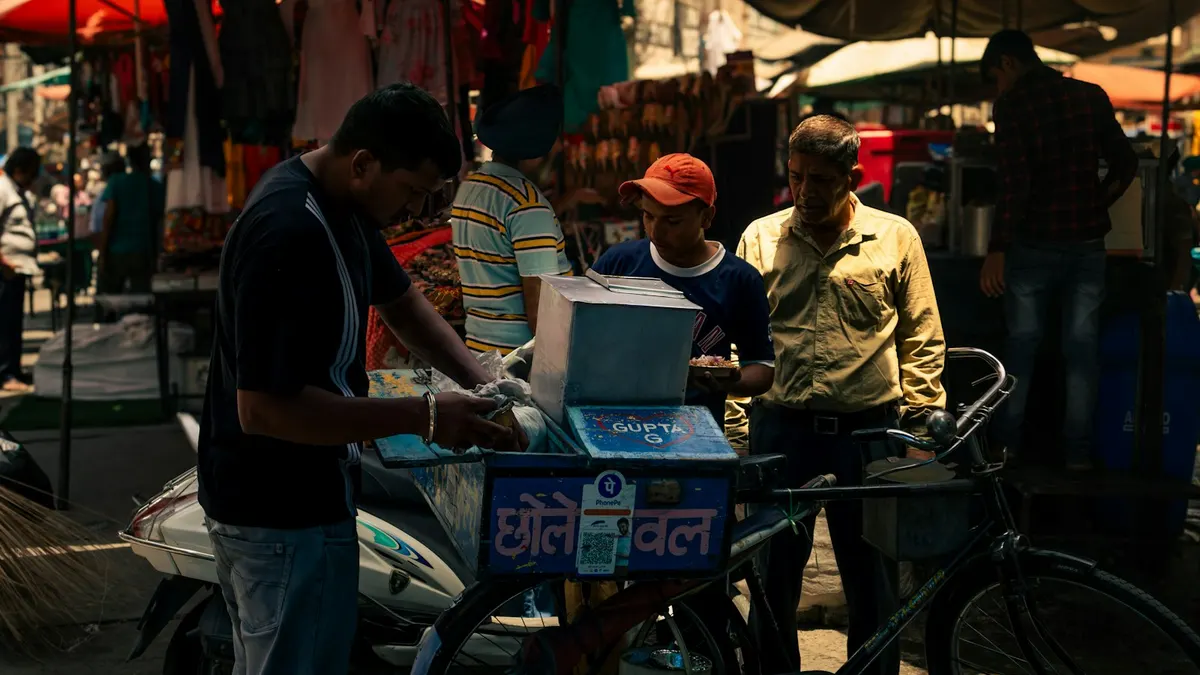 Street vendor serving customers at a market stall with a payment QR code on the front